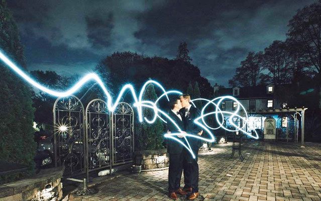 A man is standing in front of a fence with a light trail behind him.