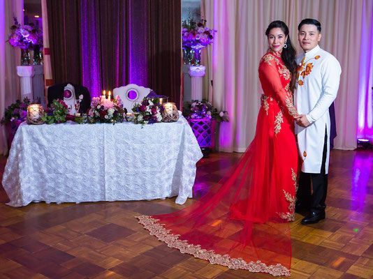 A bride and groom are posing for a picture in front of a table at their wedding reception.