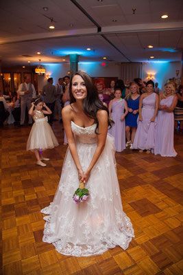 A bride in a wedding dress is throwing her bouquet at her wedding reception.