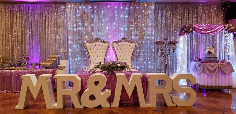 A large mr. and mrs. sign is sitting in front of a table and chairs at a wedding reception.