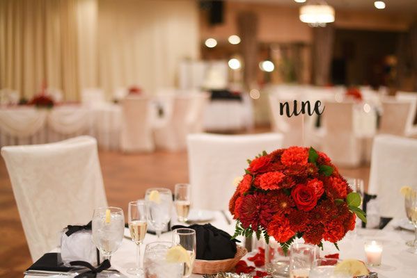 A table set for a wedding reception with a vase of red flowers on it.