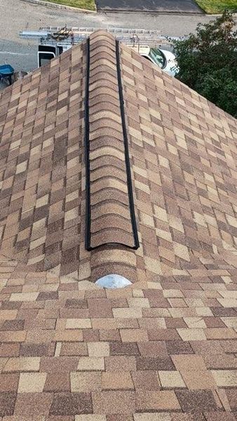 Brown shingled roof with a black ridge vent. A metal exhaust vent is visible at the bottom.