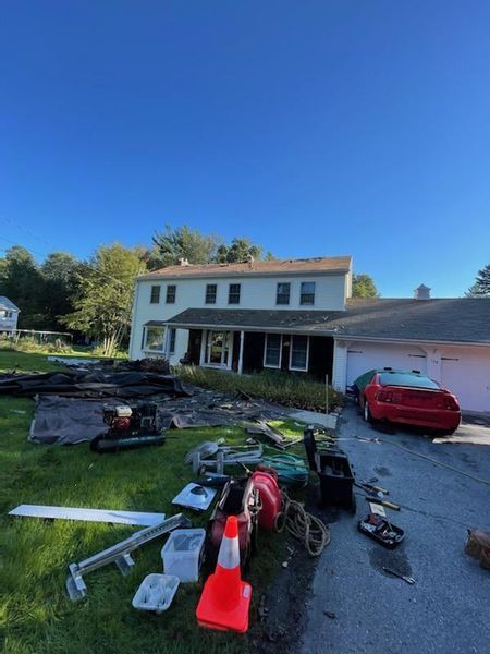 House with yard full of debris and car in driveway under clear, blue sky.