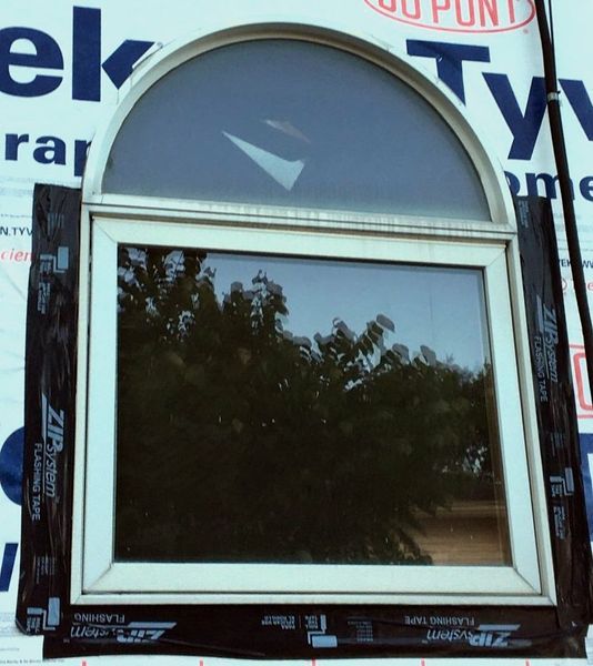 Installed white window, arched top, on exterior wall with black flashing tape.