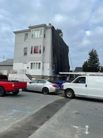 Three-story building with black tarp on the side, next to vehicles, likely after a fire.