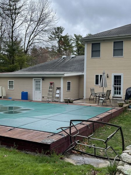 Backyard with pool covered by a tarp, house with deck, and green grass.