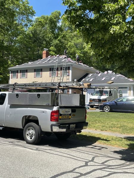 Silver truck with roofing materials, house with roof being worked on, parked on street.