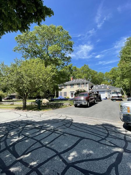 A house and driveway on a sunny day. Vehicles and trees are visible. Blue sky.