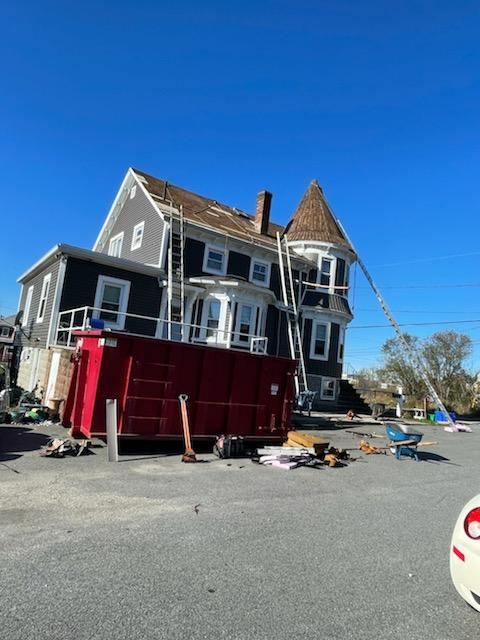 House with ladders, a red dumpster, and construction debris under a clear blue sky.