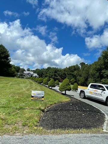 White truck on a driveway, with landscaping and sign; house on a hill, sunny blue sky.