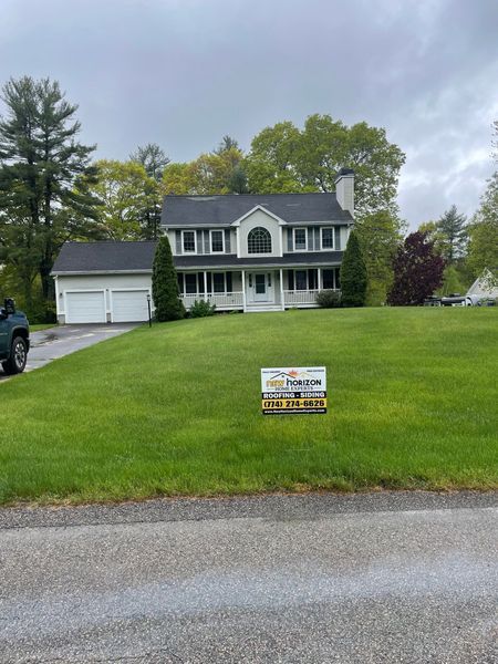 Two-story white house with attached garage, dark roof, and sign on green lawn.
