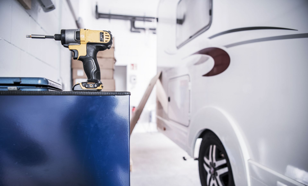 Tan and black RV parked outdoors under a blue sky, next to another RV.