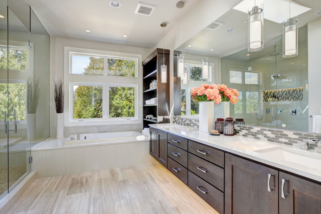 Bright modern bathroom with double vanity, large windows, glass shower, and freestanding tub