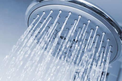 Close-up of a chrome showerhead spraying water streams against a blue background