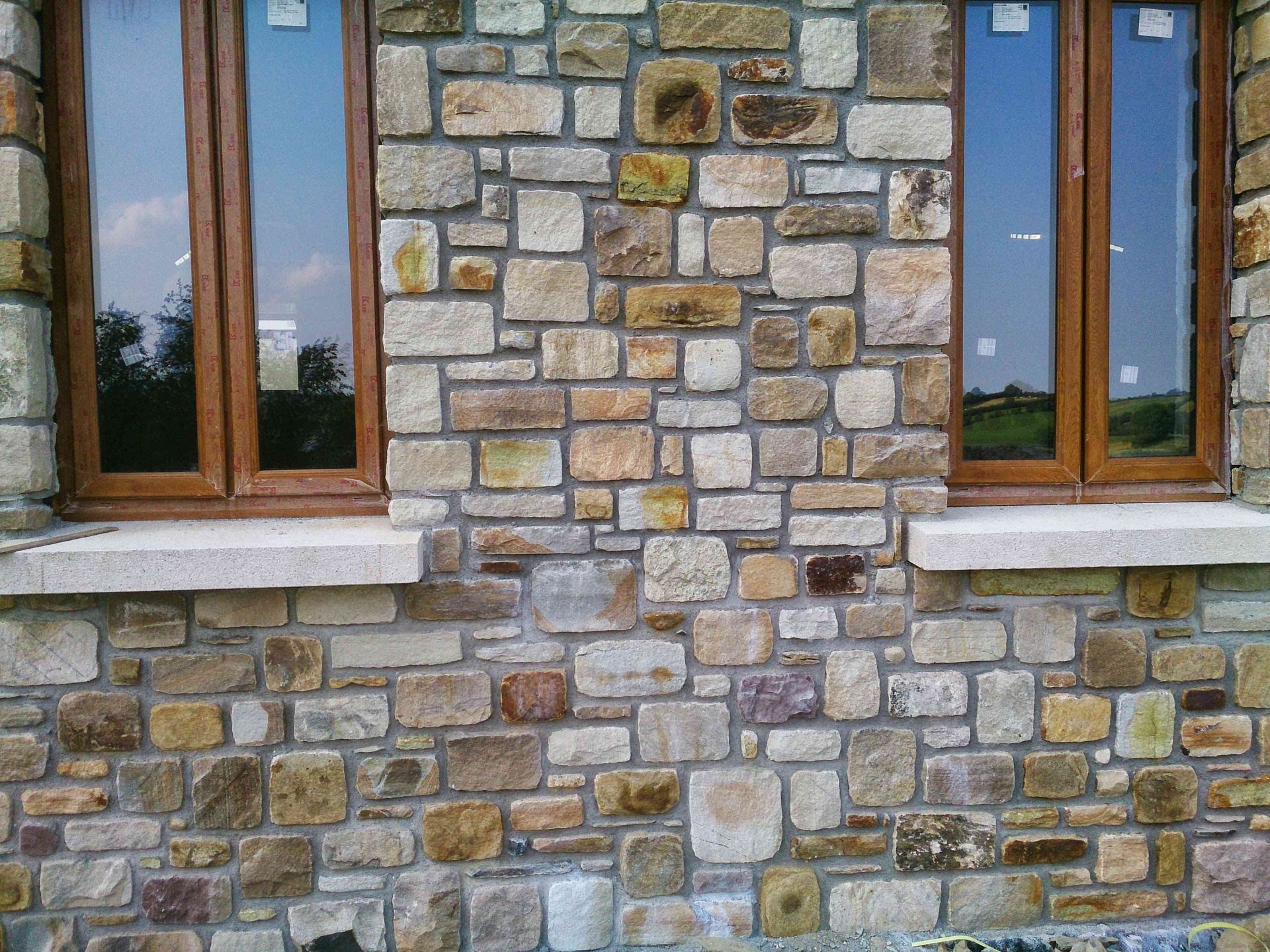 A stone wall exterior with two rectangular brown-framed windows and light-colored stone sills.