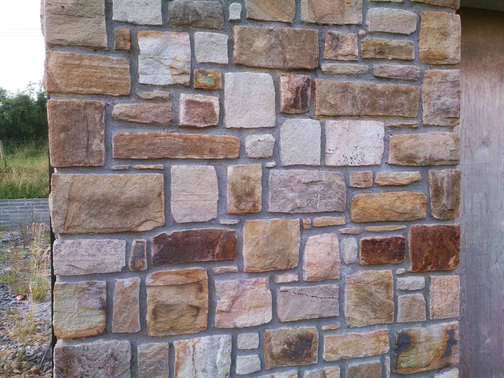 A wall constructed of natural, rectangular stones in varying shades of tan, brown, and grey with light grey mortar.