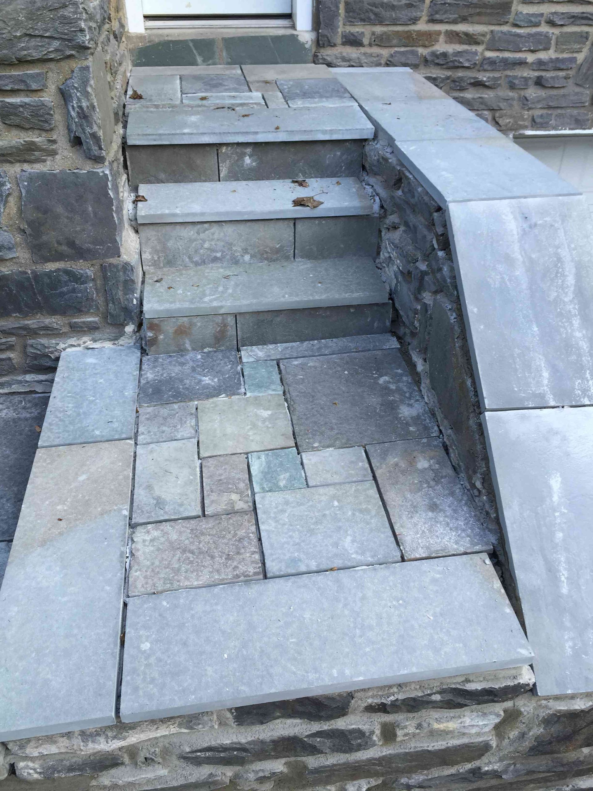 Stone steps leading to a doorway, featuring a landing area with a mix of blue-gray rectangular and square flagstones.