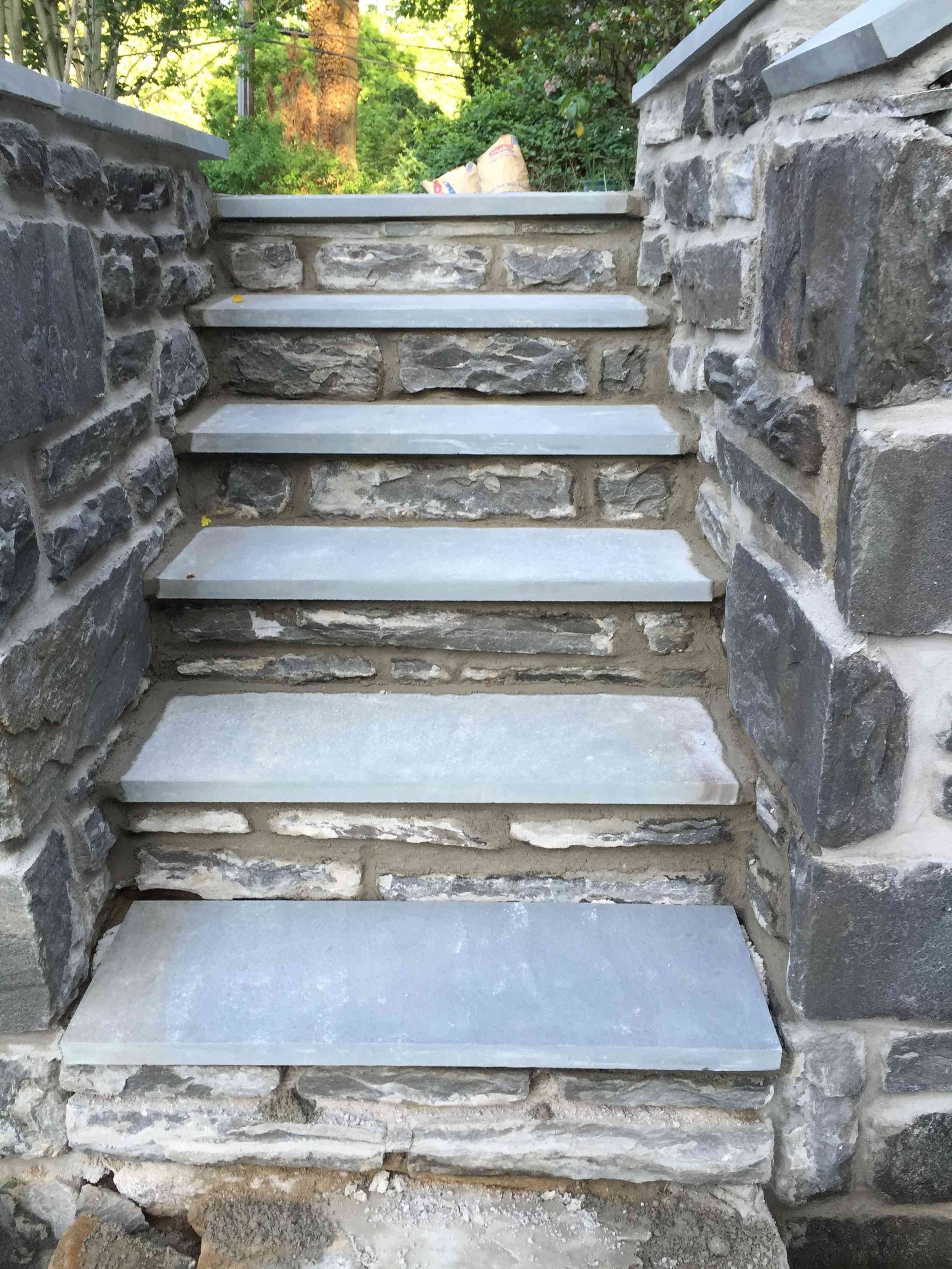 A set of stone stairs leading upward, featuring light grey stone treads and dark grey stone side walls.