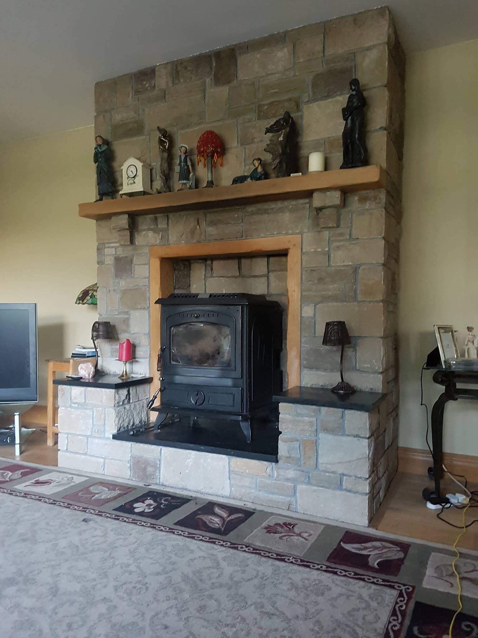 A stone fireplace with a wood-burning stove, wooden mantle, and decorative figurines in a living room.