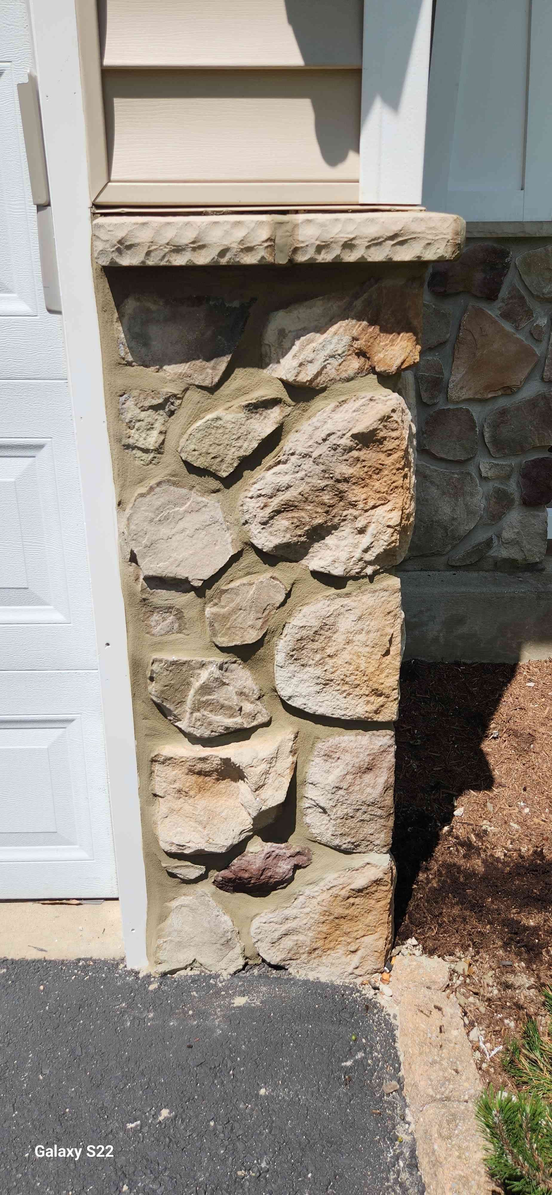 A stone pillar topped with a ledge sits beside a garage and exterior wall of a building.