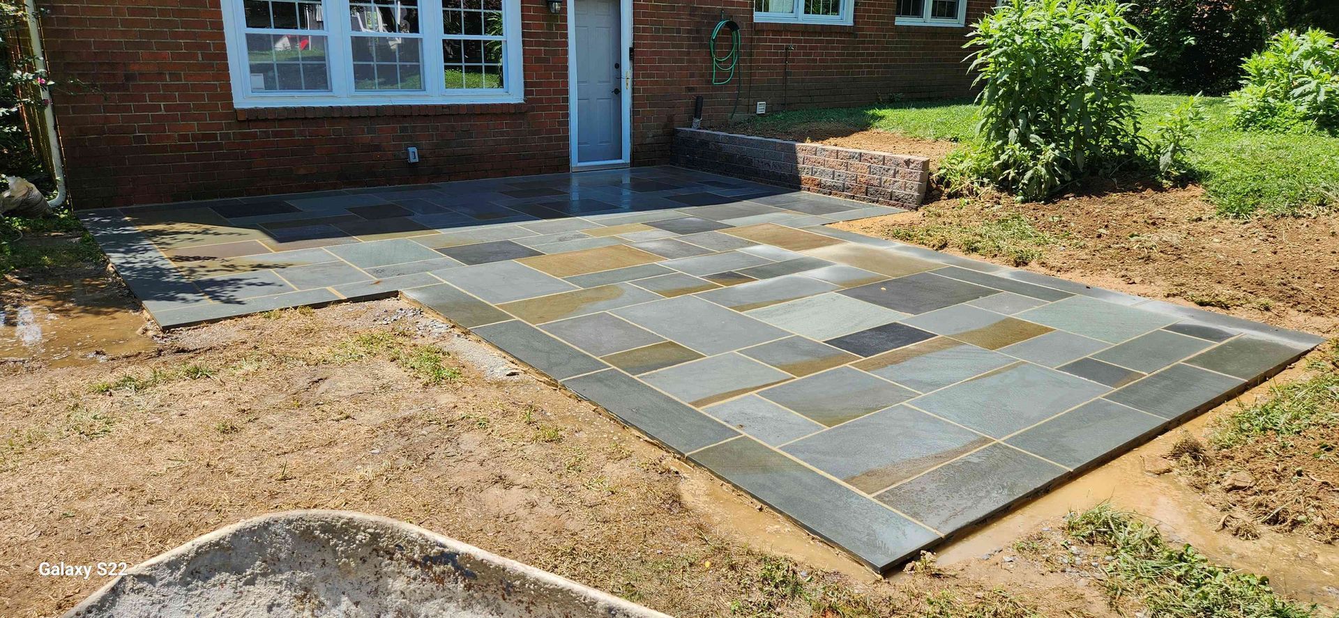 A newly installed rectangular slate patio made of varied grey and tan stone tiles next to a brick house.