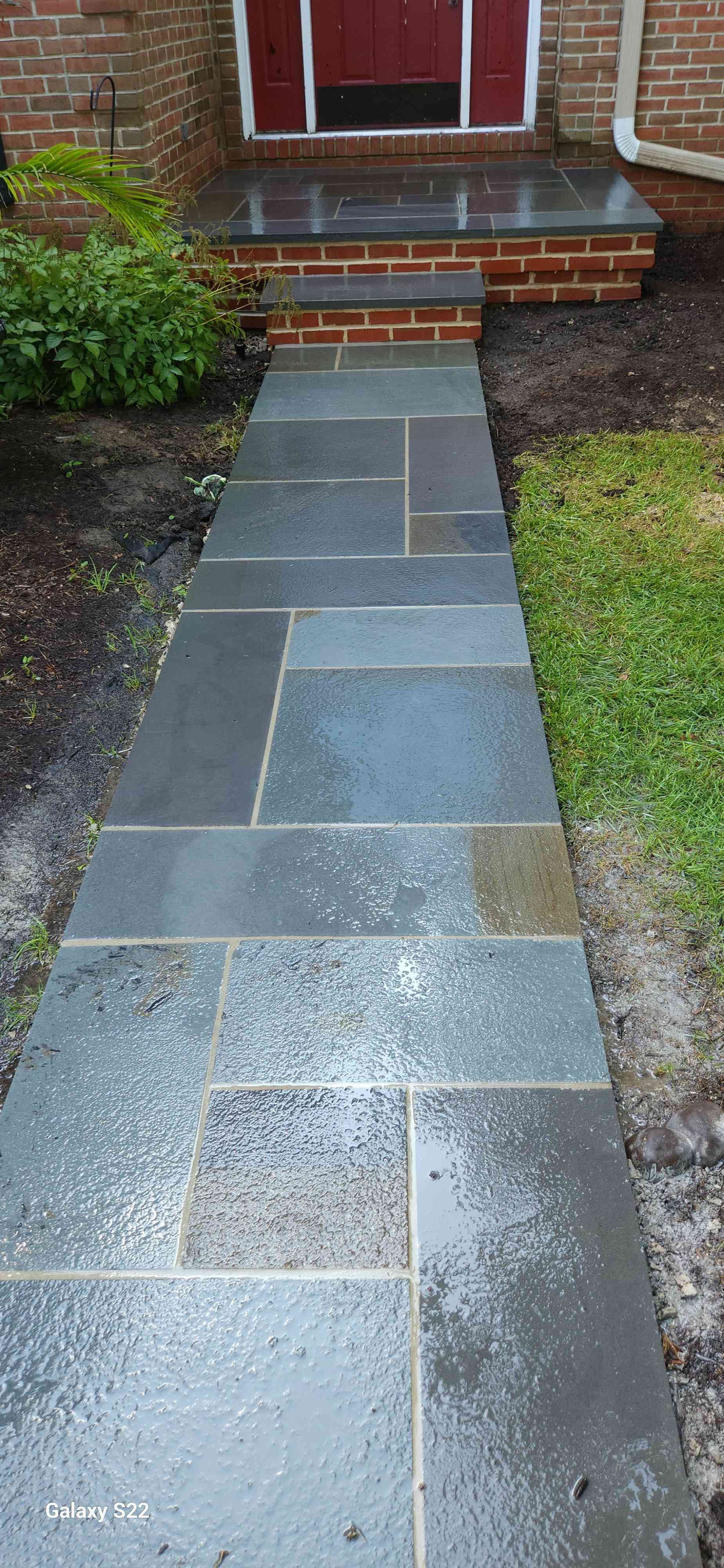 A slate stone walkway leads to brick steps in front of a house door.