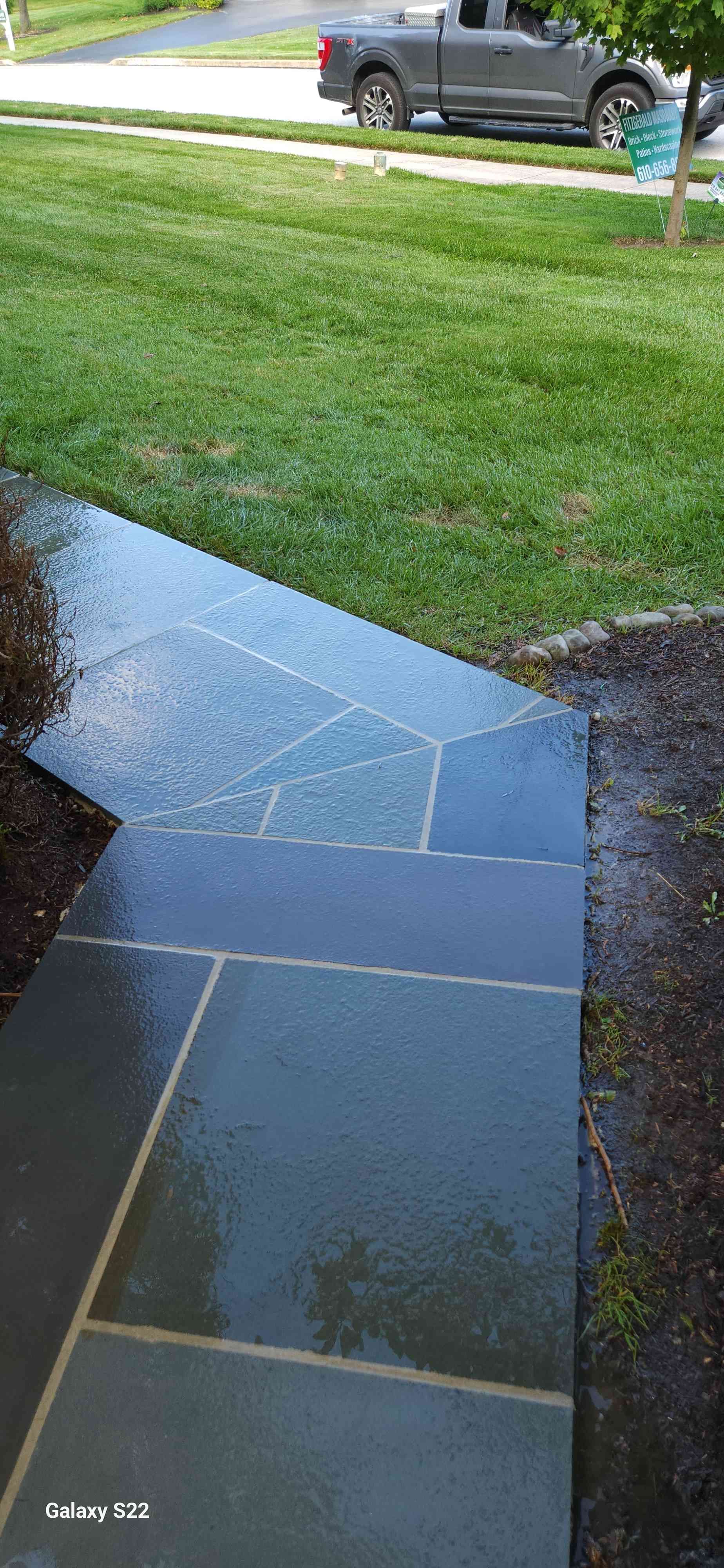 A wet stone walkway leads through a green lawn toward a parked pickup truck in the background.