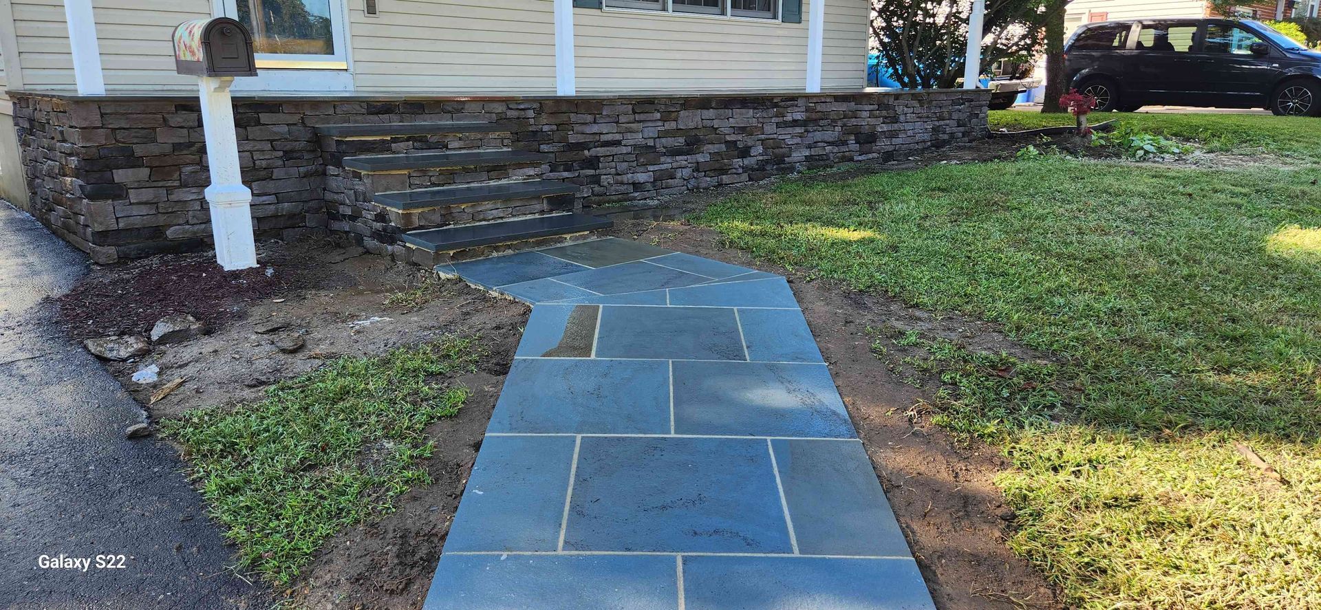 A blue stone walkway leads to stone steps and a front porch of a house with a mailbox on a white post.