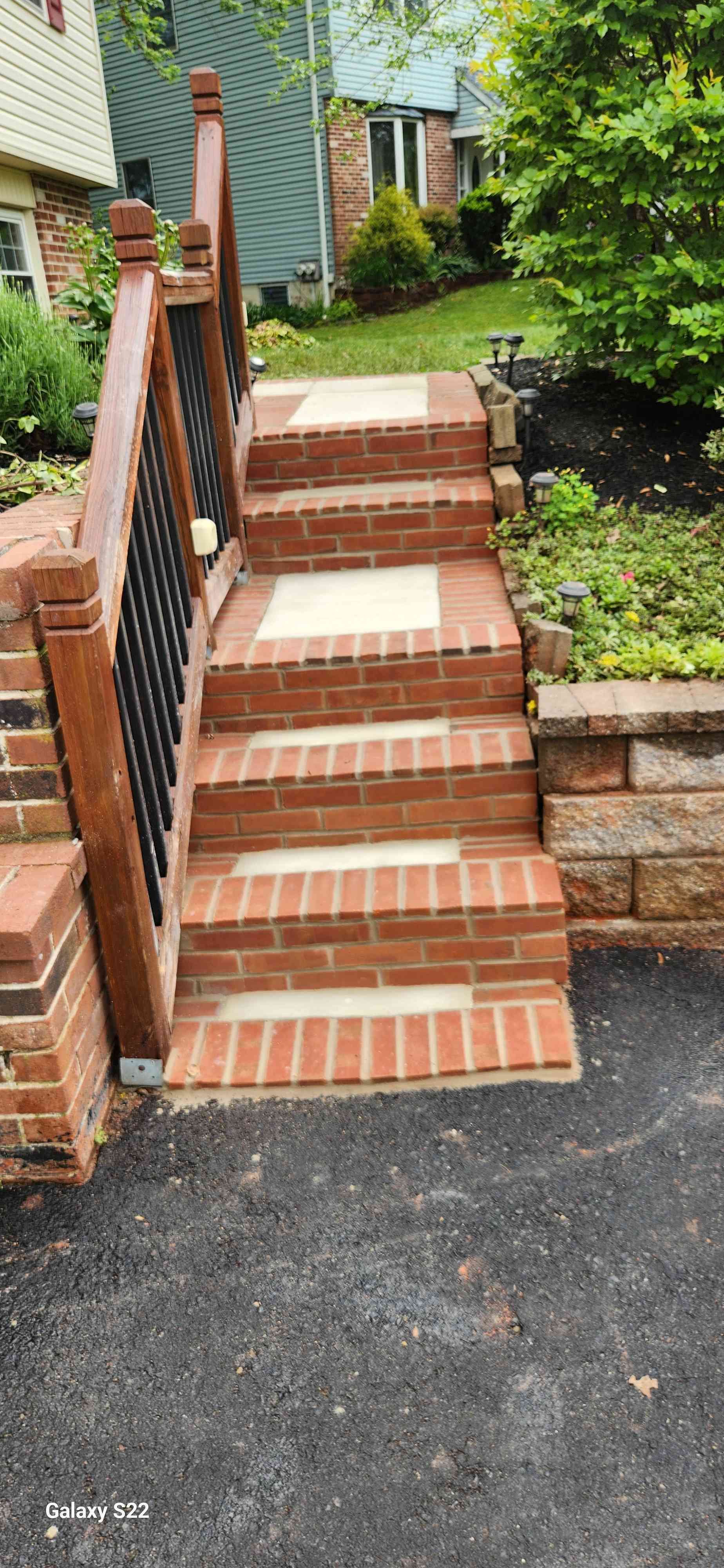 A set of outdoor red brick stairs with beige concrete treads and a wooden railing leading up to a residential home.