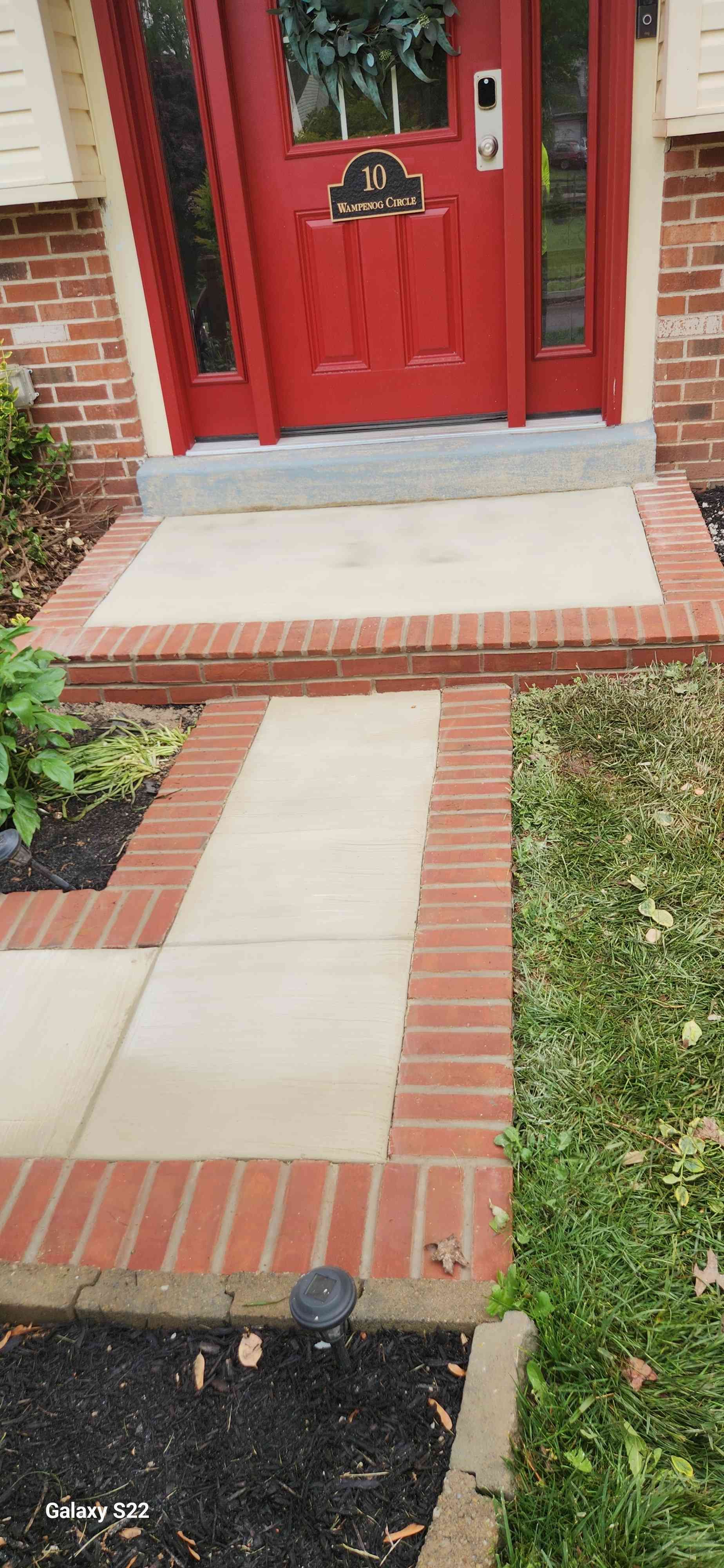 A bright red front door with a decorative cat sign, reached by a concrete walkway edged with reddish-brown bricks.