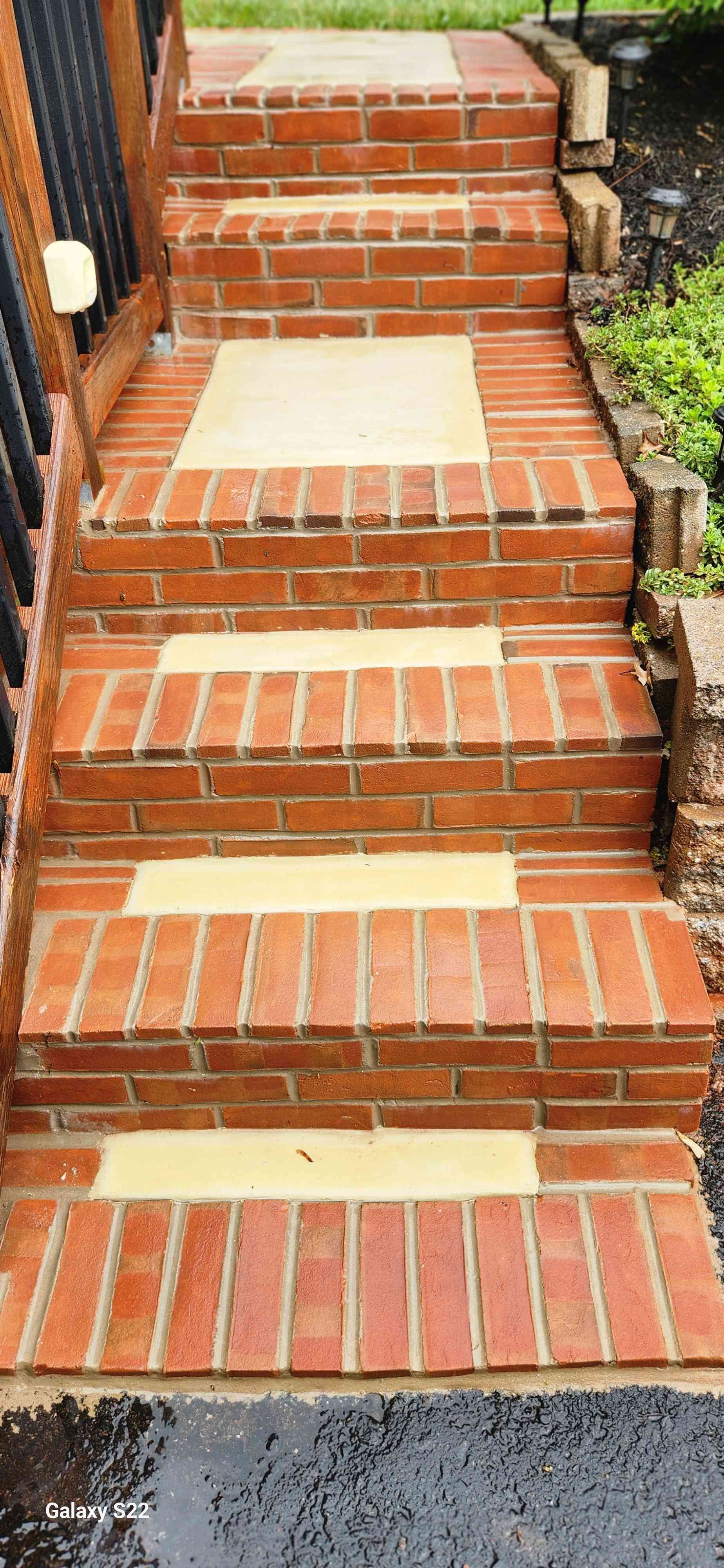 A set of outdoor brick stairs featuring light tan stone inserts on each tread, leading up to a wooden deck railing.