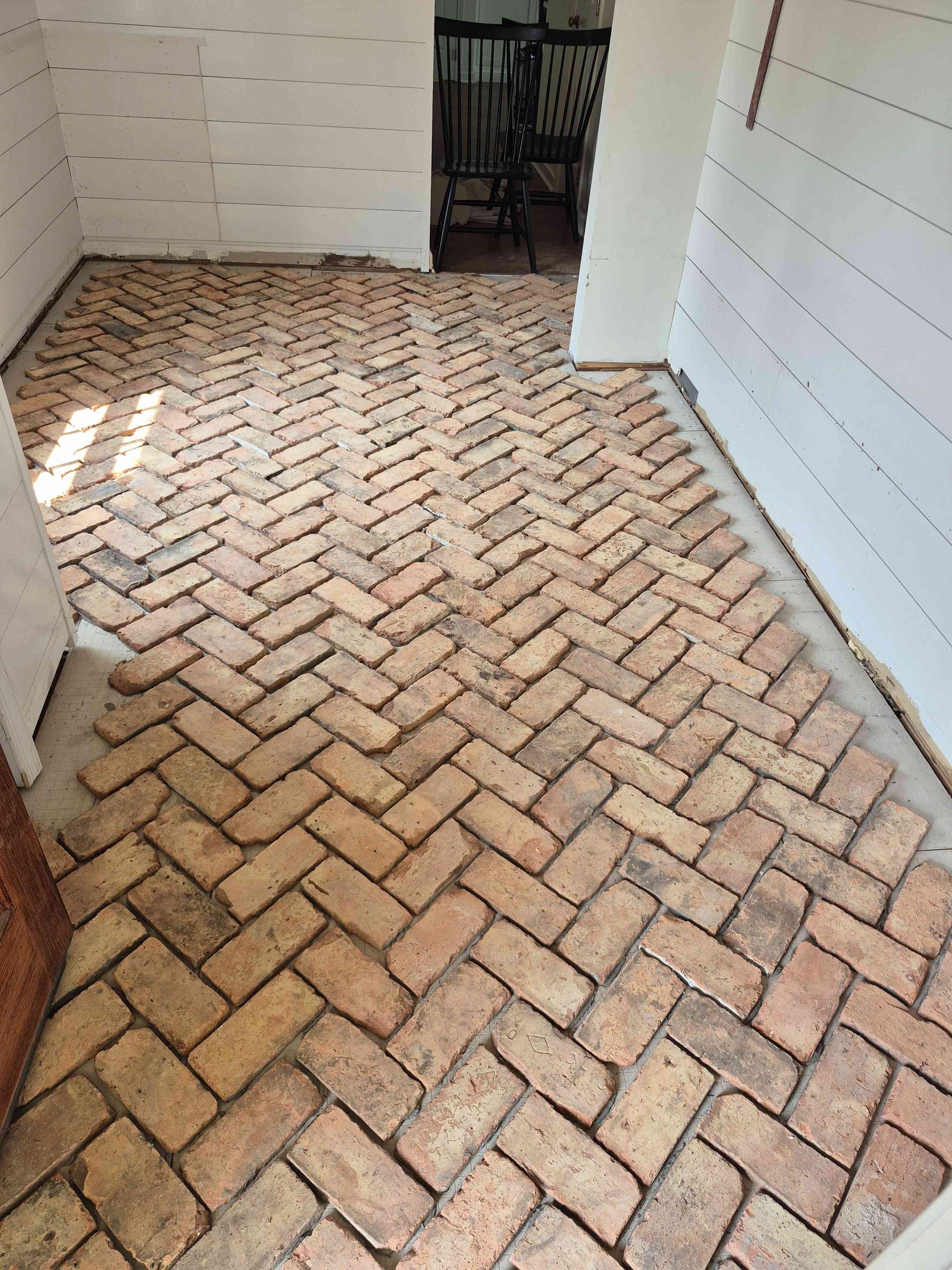An interior room with white shiplap walls and a herringbone-patterned brick floor.