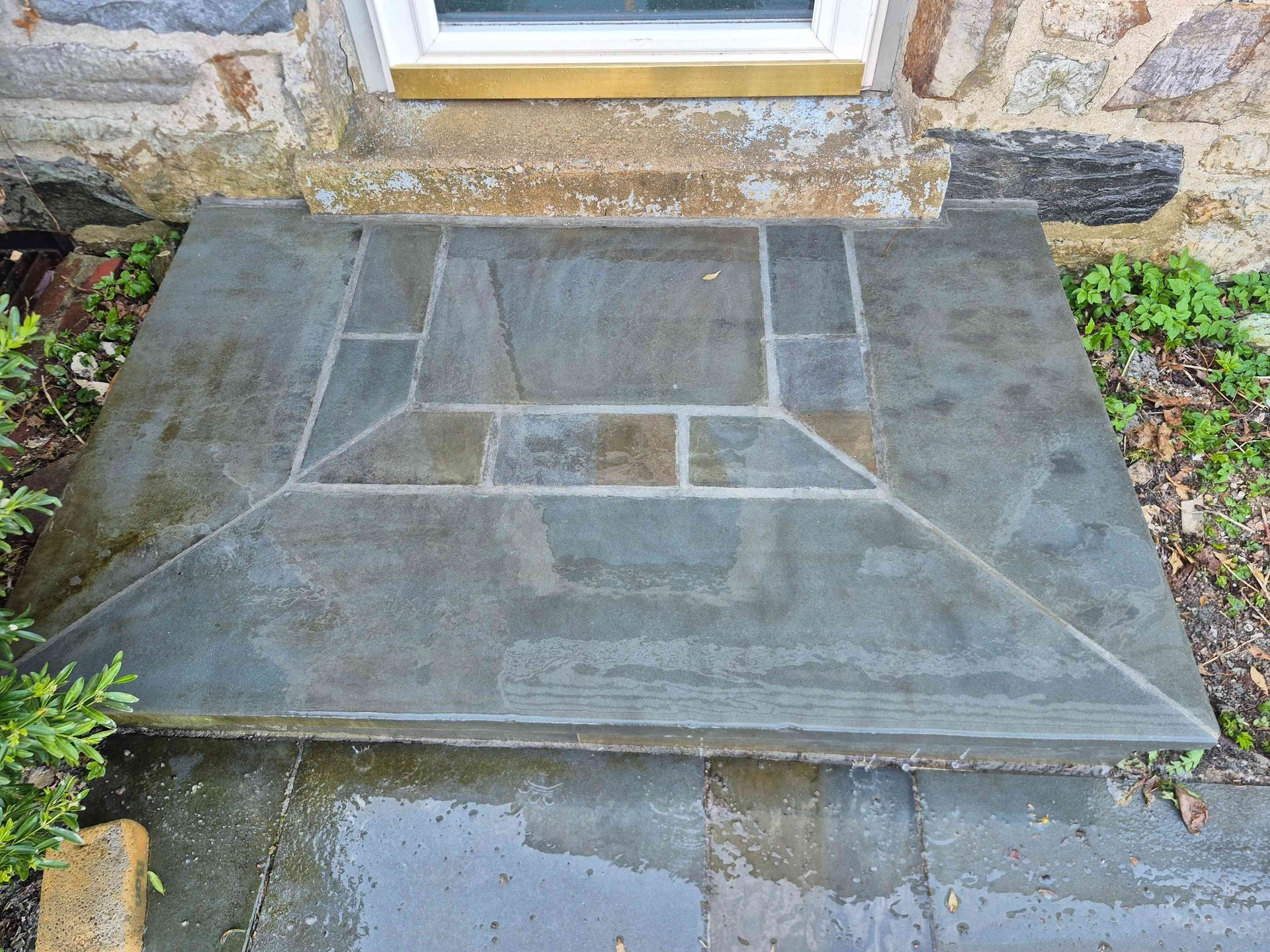 A stone step entryway featuring a decorative geometric pattern in shades of gray, brown, and blue-green slate.