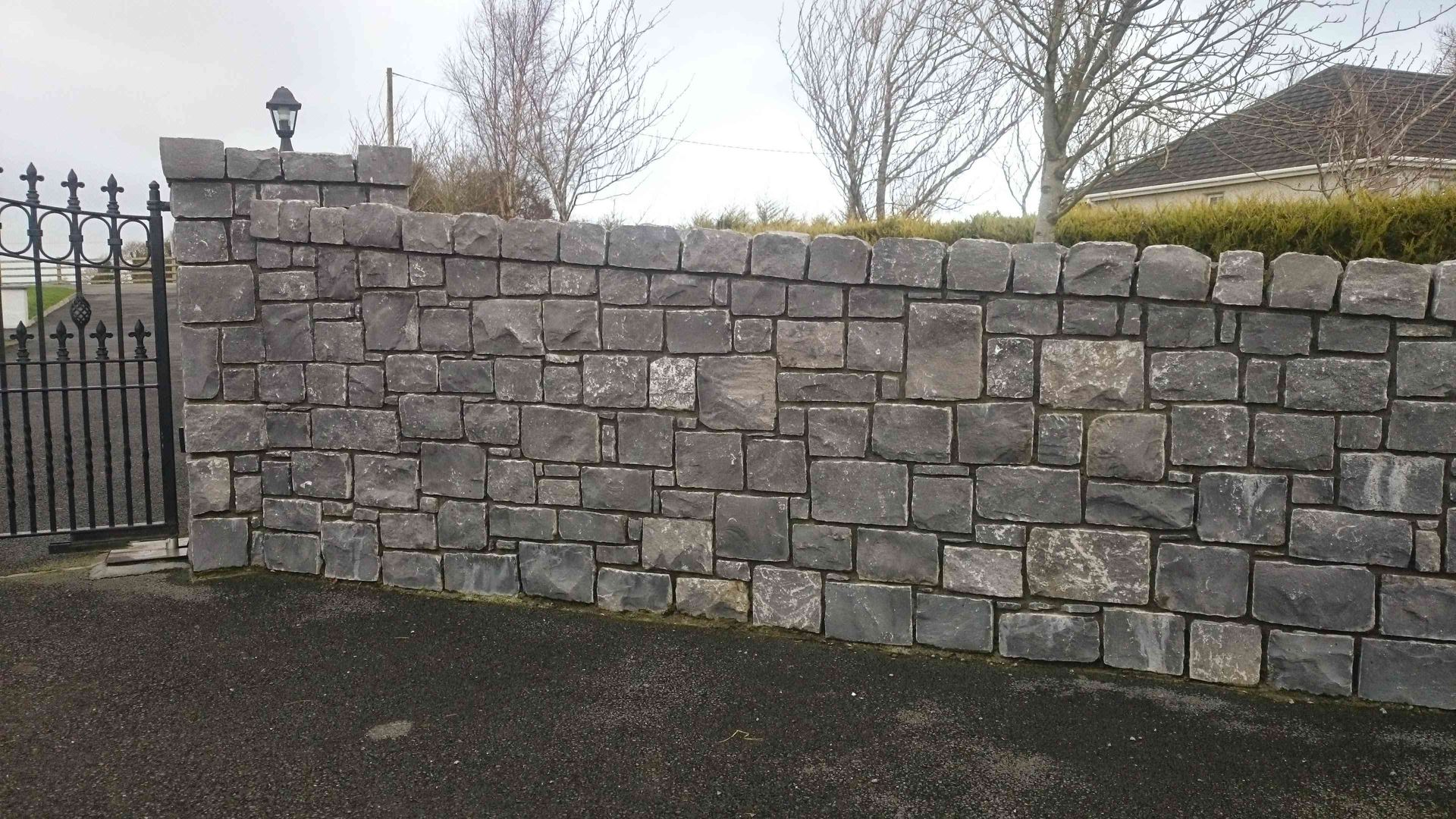 A grey stone wall with a dark metal gate on the left and trees in the background.