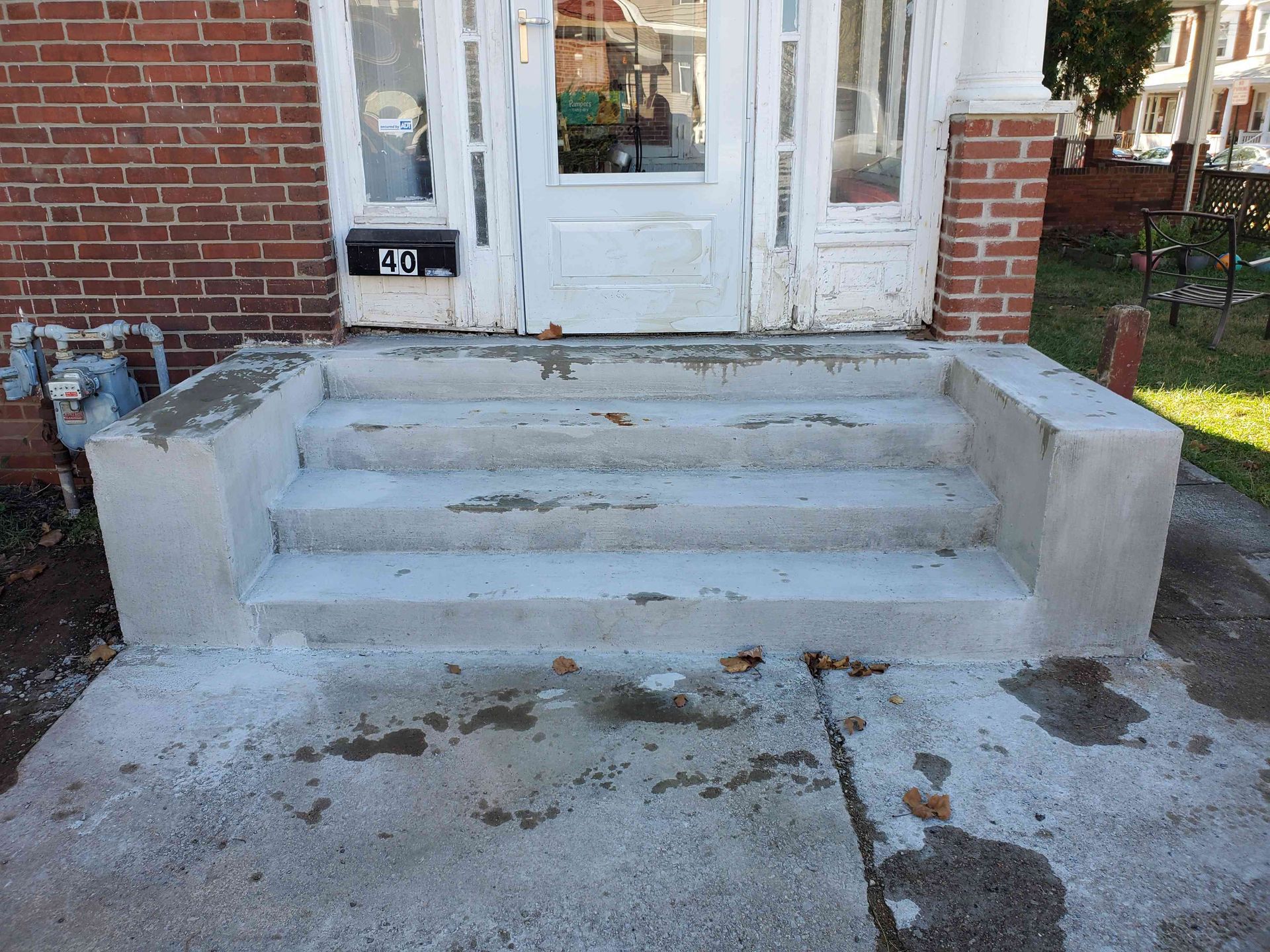 Newly parged concrete steps leading up to a white door on a brick house.