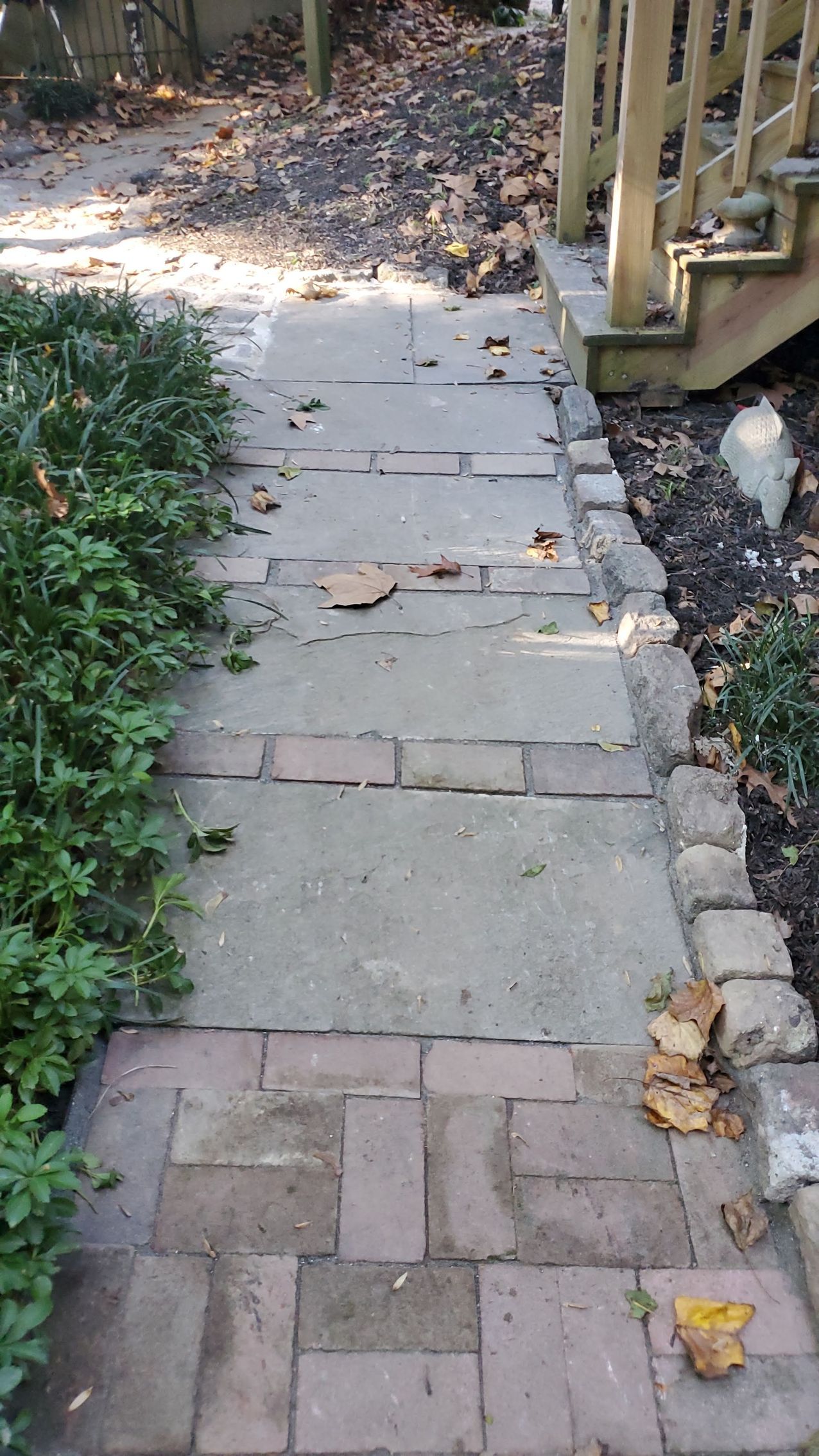 A walkway transitions from red brick pavers to large concrete slabs, leading toward wooden porch stairs outdoors.