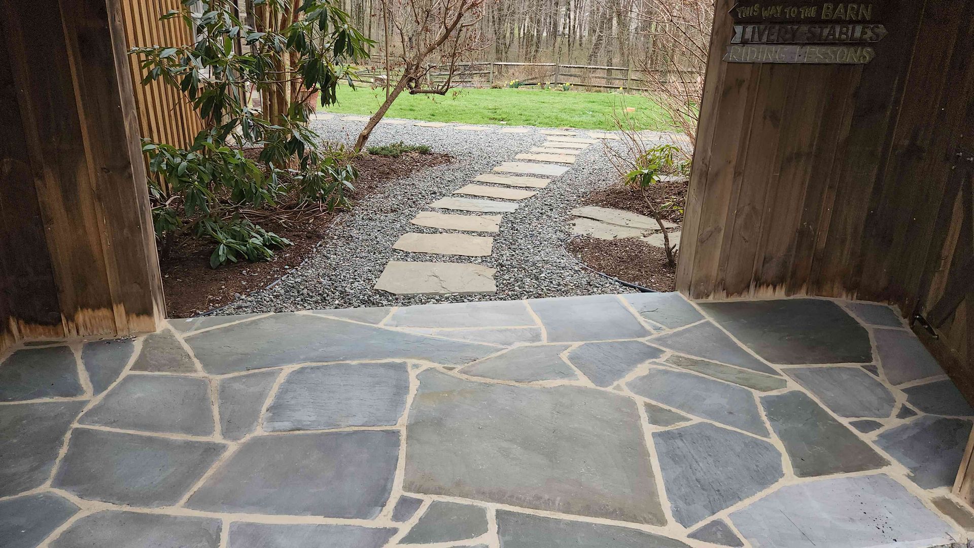A flagstone patio leads to a gravel path with stepping stones in a wooded garden setting.