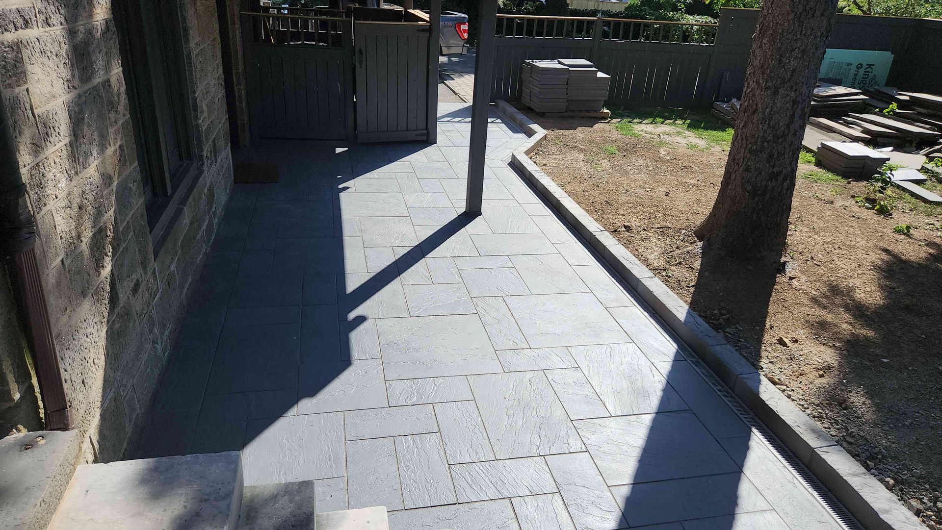 A paved patio walkway leads along the side of a stone building toward a backyard gate.