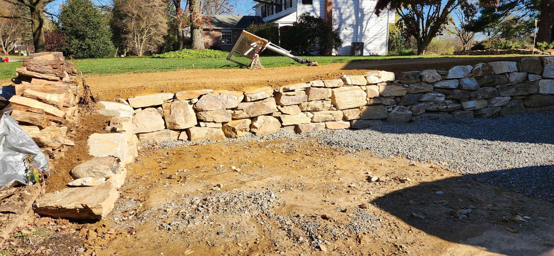 A low natural stone retaining wall under construction in a yard, with gravel and soil base in the foreground.