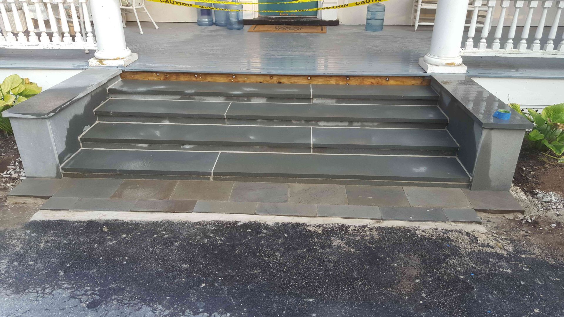 New gray stone entrance steps with matching side walls lead to a porch, situated behind a walkway and driveway.