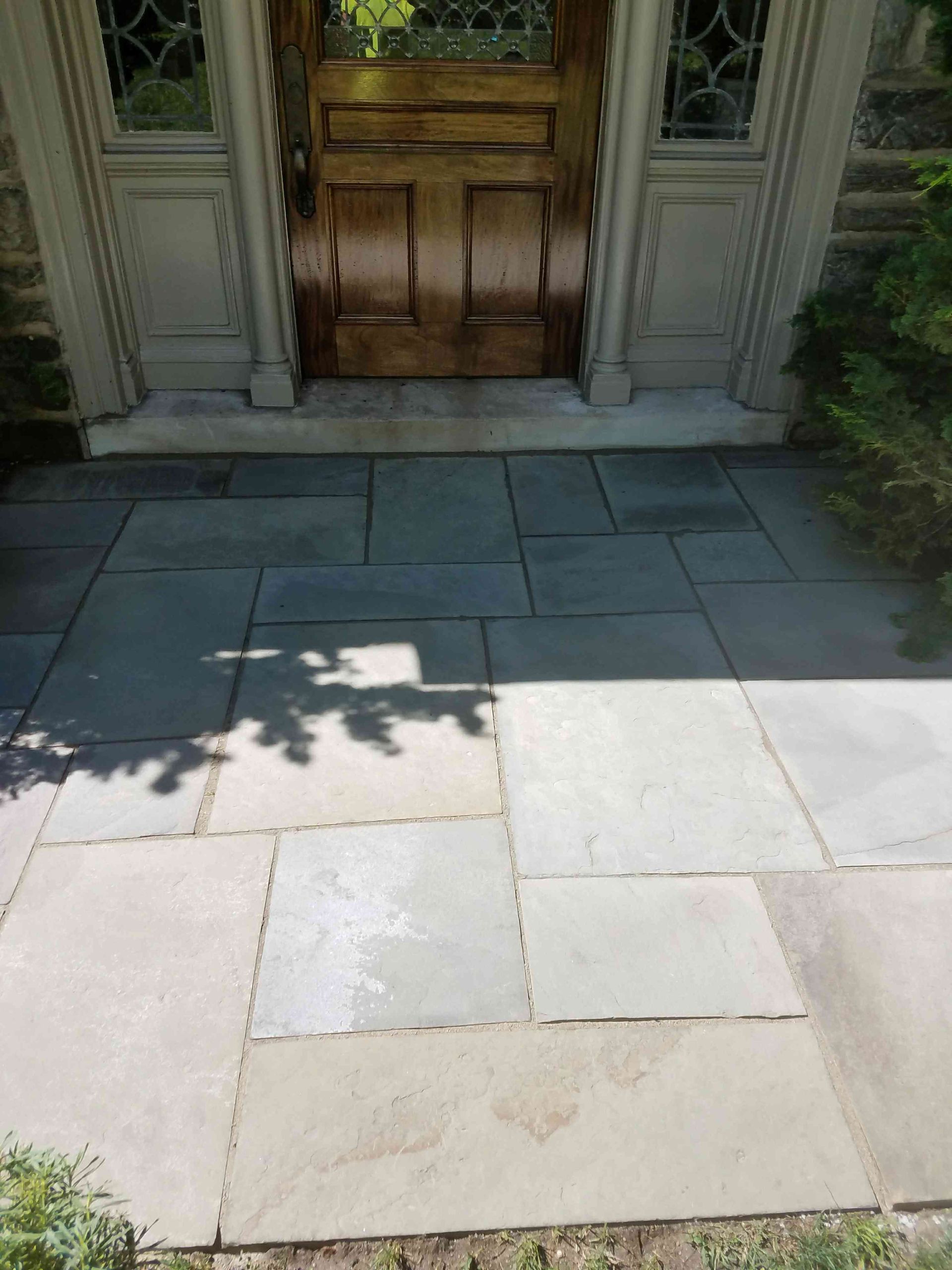A wooden front door with a decorative glass panel, set above a walkway made of large, rectangular grey stone pavers.