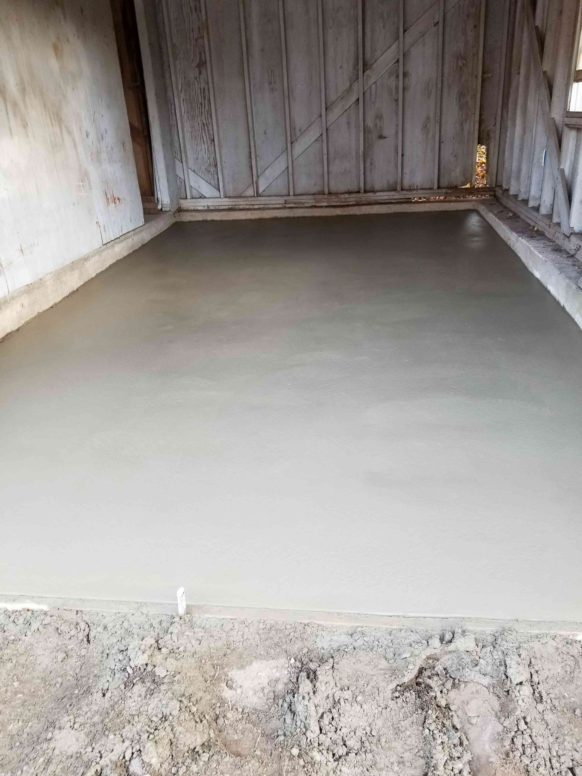 A freshly poured, smooth gray concrete floor inside a wooden shed structure.