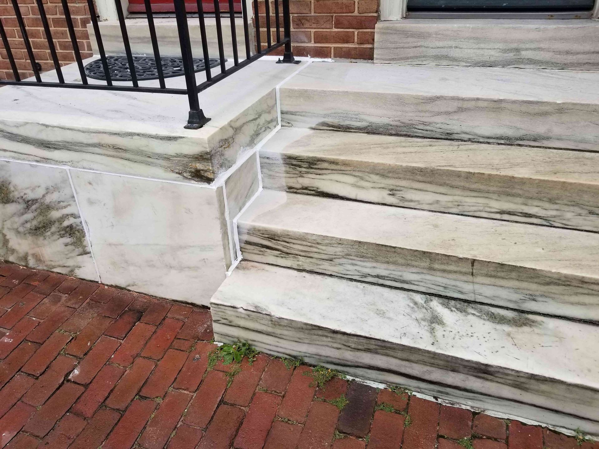 A set of stone steps leading to a brick building entrance, featuring a white metal railing and brick patio.