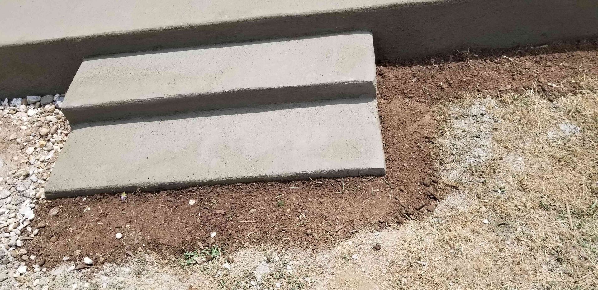 Concrete steps leading up to a building entrance, with a patch of dirt and sparse grass in the foreground.