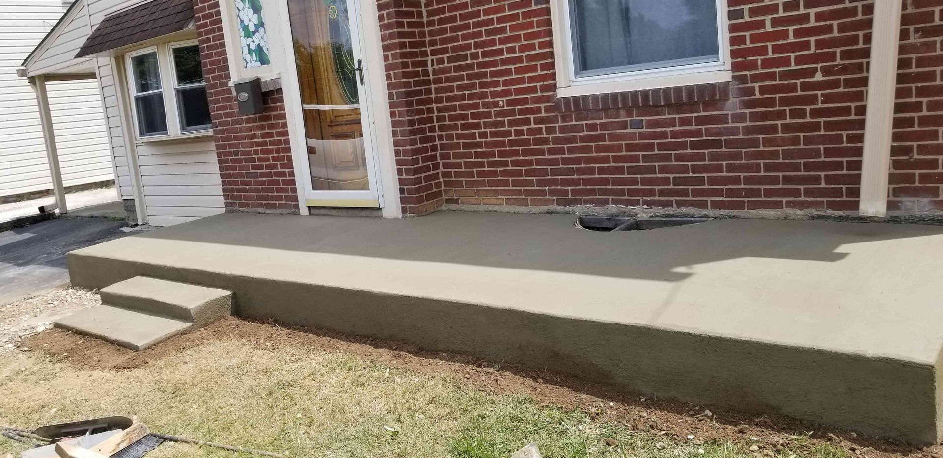 A newly poured concrete porch with two small steps in front of a red brick house.