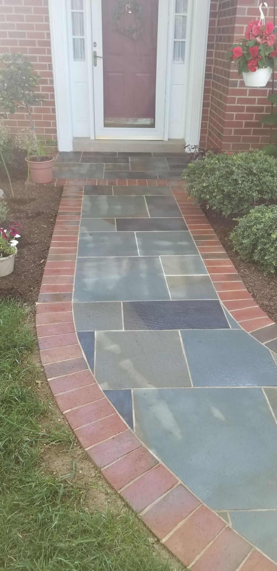 A stone walkway with a red brick border leading to a front door of a brick house.