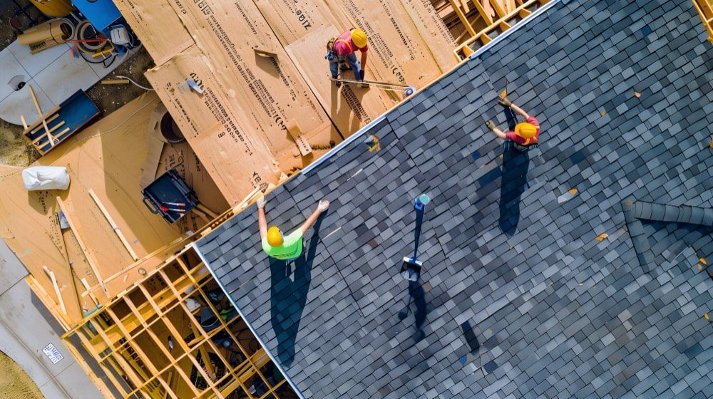 Construction workers installing roof shingles.
