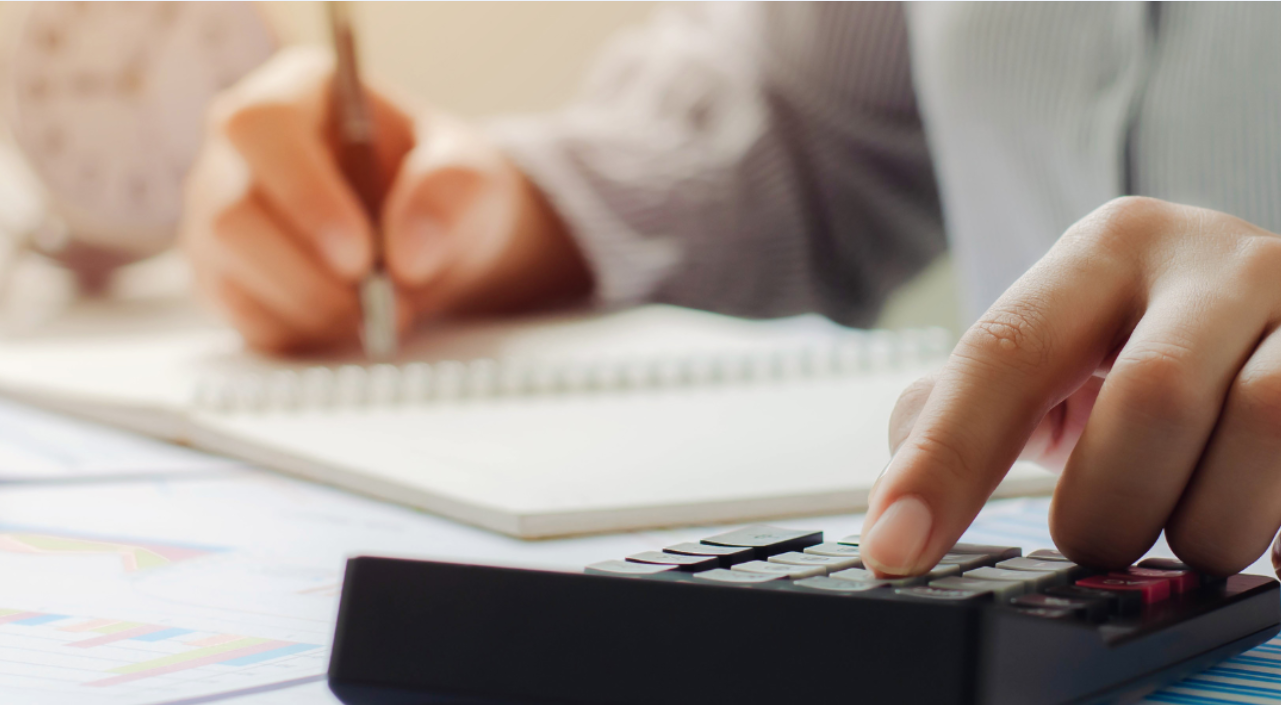 Person's hands using a calculator and writing in a notebook, focused on financial calculations.