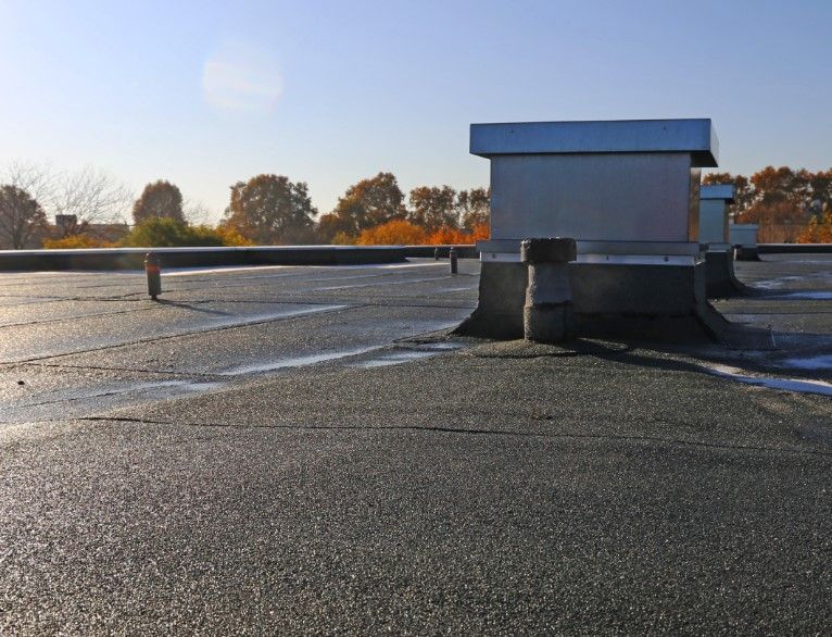 Flat commercial roof with vents under a clear sky.