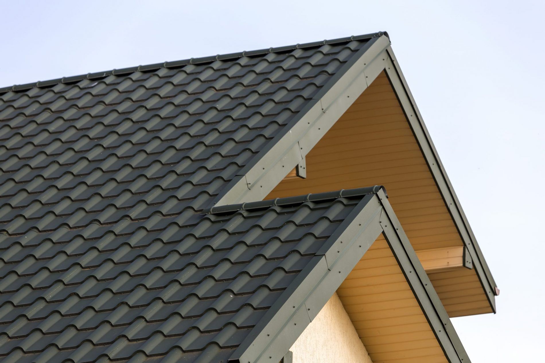Black metal roof on a light-colored building with a blue sky background.